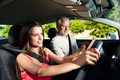 A woman driving while an older man watches.