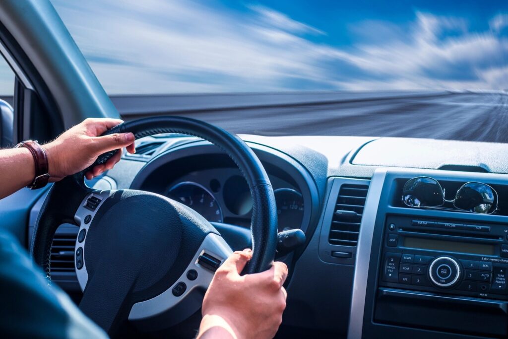 A person is driving in the car while holding on to the steering wheel.