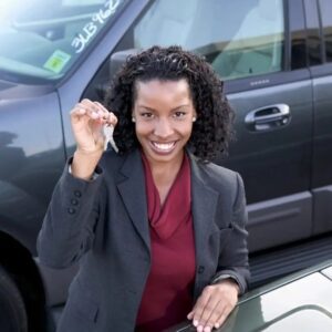 A woman holding up a key in front of her car.