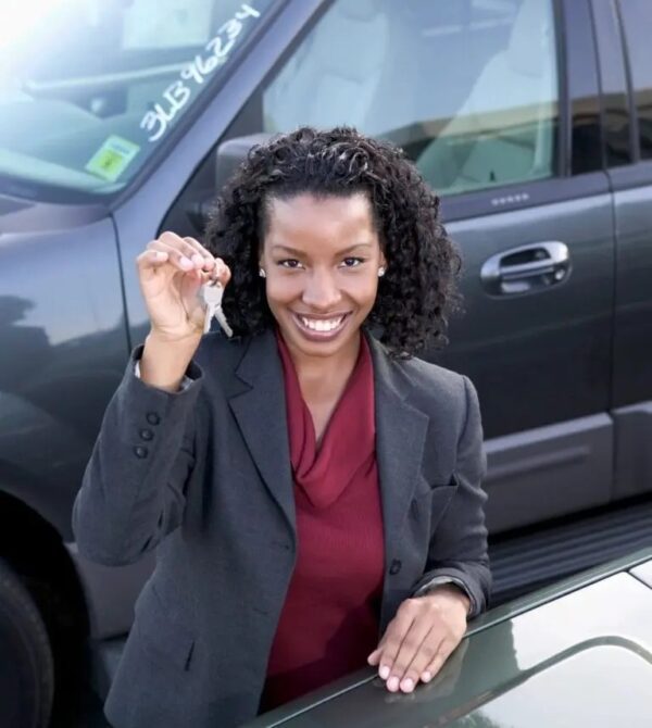 A woman holding up a key in front of her car.