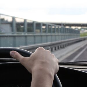 A person driving on the road with their hand on the steering wheel.