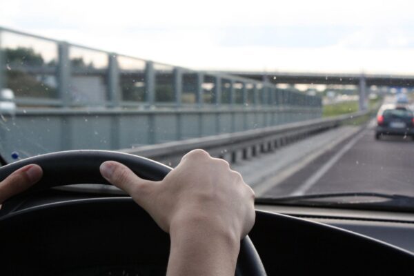 A person driving on the road with their hand on the steering wheel.